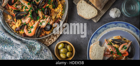 Les plaques avec la paella sur la table en pierre avec différents accessoires écran large Banque D'Images