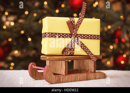 Cadeau enveloppé de rubans pour noël allongé sur traîneau en bois et l'arbre de Noël avec des lumières en arrière-plan Banque D'Images