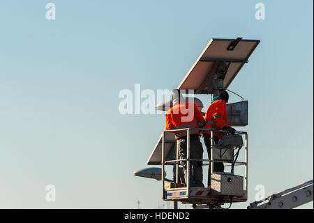 Les travailleurs de lever la benne lors de la maintenance de streetlight alimenté par un panneau solaire. Banque D'Images