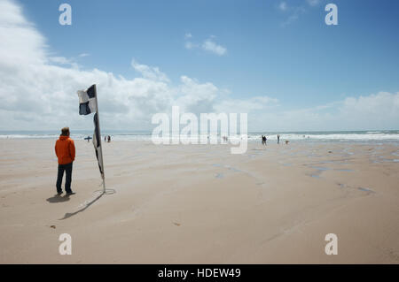 Un homme debout par un sauveteur à carreaux noirs et blancs la sécurité à la plage de la RNLI maintien du pavillon un belvédère sur la plage de la baie de Croyde Banque D'Images