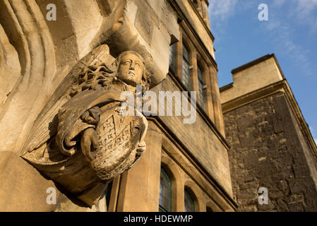 Sculpture gothique médiévale représentant un ange aux cheveux longs tenant un bouclier gravés sur pierre brune sur l'extérieur d'un bâtiment ancien Banque D'Images