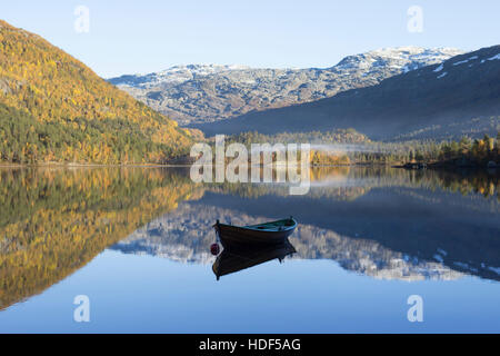 Un vieux bateau aviron calme reposant sur un lac en automne. Un ciel bleu, montagne enneigée tops et un petit brouillard sur la rive opposée. Banque D'Images