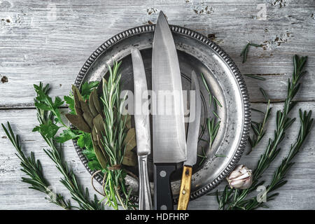 Plaque de métal avec des couteaux et des herbes sur la vue de dessus de table blanc Banque D'Images