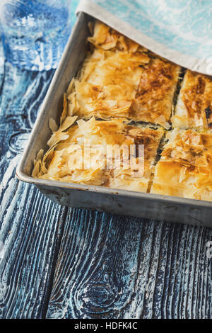 Spanakopita tarte grecque dans le métal sur le pan de bois bleu table verticale Banque D'Images