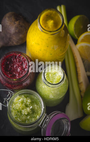 Bouteilles et pot de smoothie et de différents ingrédients sur la table en pierre sombre Banque D'Images