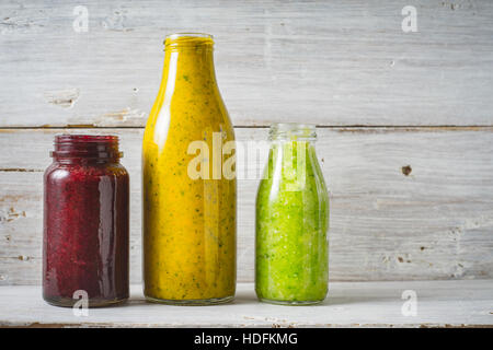 Vert, jaune et rouge dans la bouteille en verre de smoothie sur le fond en bois blanc Banque D'Images