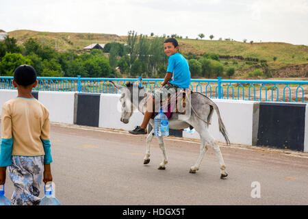 TURBAT, KAZAKHSTAN - 21 juillet : deux enfants de transporter les bouteilles en plastique d'eau sur la route par l'âne. Juillet 2016 Banque D'Images