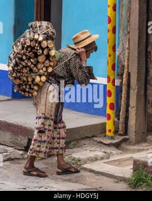 Un pauvre homme maya en haillons vêtements traditionnels porte une lourde charge de bois avec un portage à San Pedro la Laguna, Guatemala. Bleu peint de couleurs vives Banque D'Images