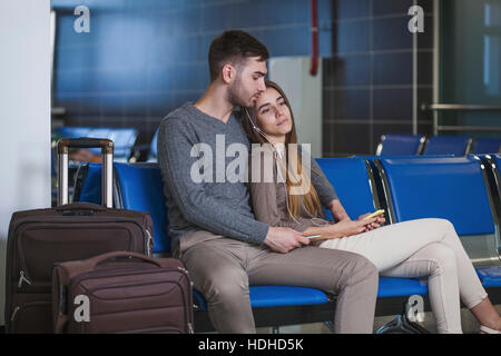 Jeune couple à l'écoute de la musique sur téléphone mobile lors de l'attente dans l'aéroport Banque D'Images