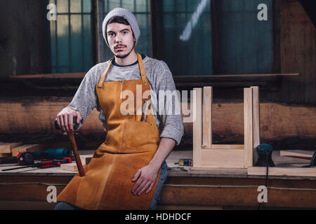 Portrait de carpenter holding hammer alors qu'il était assis sur un banc à l'atelier Banque D'Images