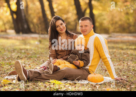 Portrait de parents assis avec mignon bébé garçon dans le parc en automne Banque D'Images