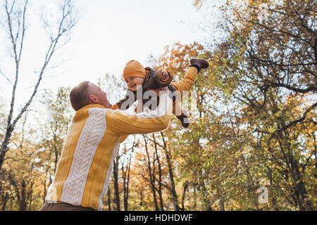 Low angle view of cheerful man lifting baby boy au parc au cours de l'automne Banque D'Images