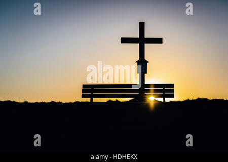 Silhouette de croix par banc contre ciel clair au lever du soleil Banque D'Images