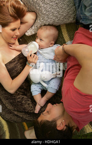 Directement au-dessus de shot of woman nourrir bébé garçon avec bouteille tandis que man lying on bed at home Banque D'Images