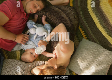 Directement au-dessus de shot of woman nourrir bébé garçon avec bouteille tandis que man relaxing on bed at home Banque D'Images