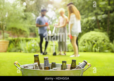 Les bouteilles de bière dans le godet tandis que friends enjoying barbecue party en arrière-plan à la cour Banque D'Images