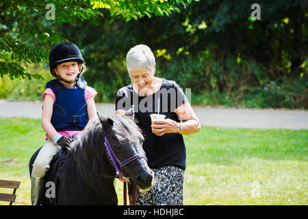 Femme et fille blonde wearing riding hat assis sur un poney. Banque D'Images