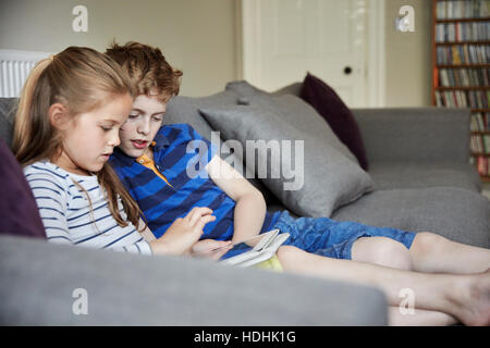 Deux enfants assis le partage d'une tablette numérique à regarder l'écran. Banque D'Images