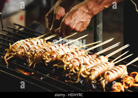 La préparation de l'alimentation de rue à l'extérieur en pays asiatique, grillades bbq calamars sur des bâtons Banque D'Images