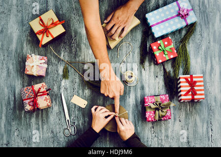 Capture d'un grand angle d'une jeune femme de race blanche et un jeune homme de race blanche, cadeaux sur une table en bois gris rustique plein de cadeaux et de brindilles et naturel Banque D'Images