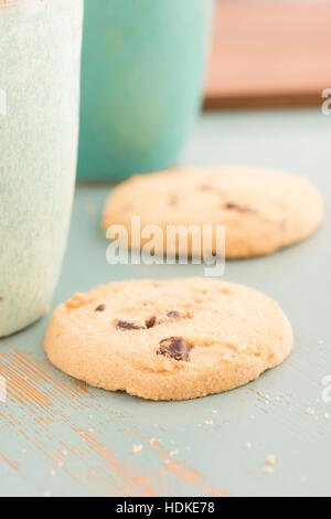 Cookies aux pépites de chocolat et de tasses de café ou de thé. Un aliment sucré, un dessert ou un en-cas. Les biscuits sont servis sur une table de cuisine. Banque D'Images