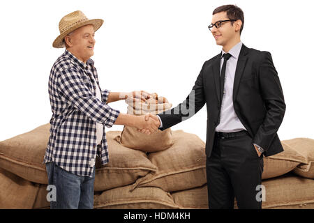 Agriculteur et un businessman shaking hands en face d'un tas de sacs de toile remplis de pommes de terre isolé sur fond blanc Banque D'Images