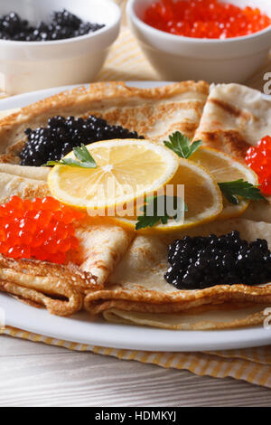 Crêpes minces avec du caviar rouge et noir sur une plaque verticale, close-up Banque D'Images