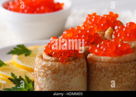 Rouleaux de crêpes farcies au caviar rouge sur une plaque horizontale de macro. Banque D'Images