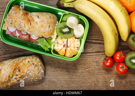 Lunch sur table en bois. Sandwich au jambon et fruits en boîte en plastique Banque D'Images