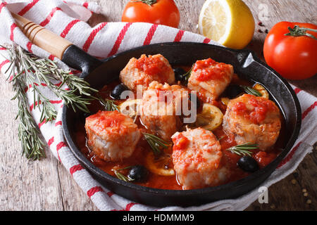 Morceaux de poissons en sauce tomate dans une casserole et les ingrédients sur la table horizontale. Banque D'Images