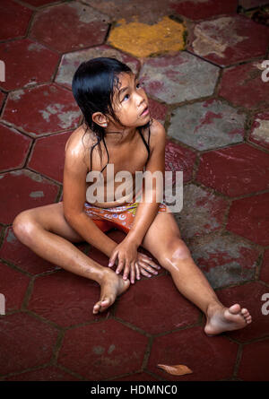 Un jeune enfant Khmer cambodgien est assis sur des pavés humides jouant dans la pluie à Siem Reap, Royaume du Cambodge. Banque D'Images