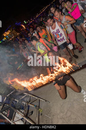 Une partie goer rejoint dans des limbes danse sous un poteau incendie lors d'une Full Moon Party à Haad Rin beach lever du soleil sur l'île de Kho Phag Nang Thaïlande Banque D'Images