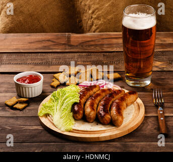 Saucisses grillées avec verre de bière, les croûtons et le chou chinois sur table en bois Banque D'Images