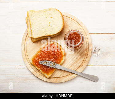 Pot de confiture de pêches avec du pain sur la table en bois blanc, en vue de dessus d'arrière-plan Banque D'Images