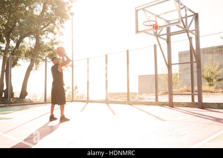 Photo de joueur de basket qui pratique dans la rue avec panier de basket-ball. À la recherche au cerceau. Banque D'Images