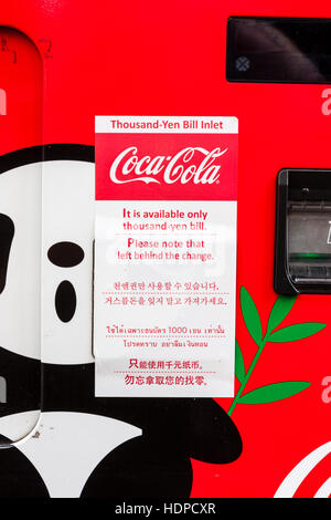 Le Japon. Signe japonais-anglais, 'Veuillez noter gauche derrière le changement' sur le coca-cola distributeur automatique. Panda cartoon. Banque D'Images