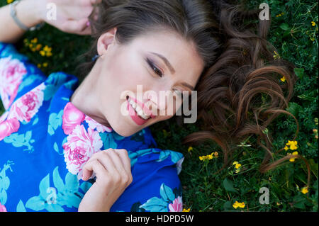 Belle femme heureuse couché dans l'herbe avec des fleurs jaunes Banque D'Images