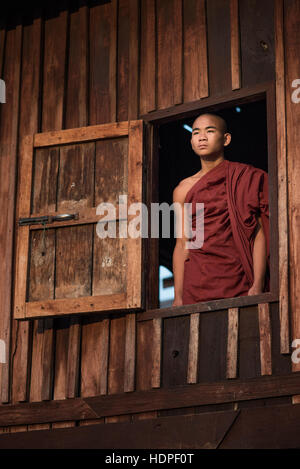 Portrait d'un jeune moine bouddhiste debout par une fenêtre du monastère en bois de Shwe Yan Pyay à Nyaungshwe, Myanmar. Banque D'Images