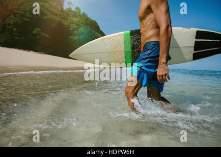 Cropped shot of young male surfer holding surf board sortant de l'océan. Homme de race blanche avec une planche de surf qui sortent de la mer. Banque D'Images