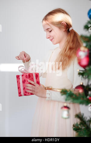 Happy girl déballage cadeaux de Noël debout derrière un arbre Banque D'Images