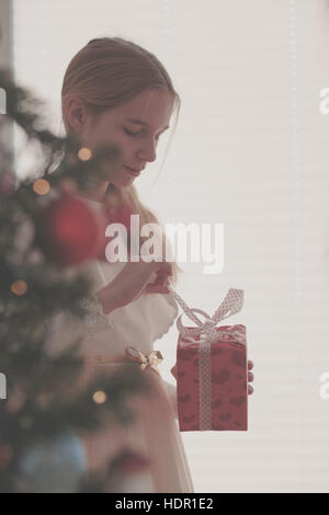 Girl déballage cadeau de Noël debout derrière un arbre Banque D'Images