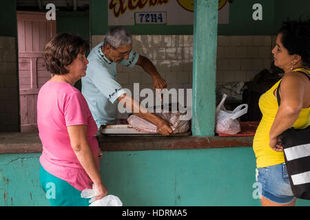 Women chatting alors que boucher ouvre sac de viande à Vinales, ration shop à Cuba Banque D'Images