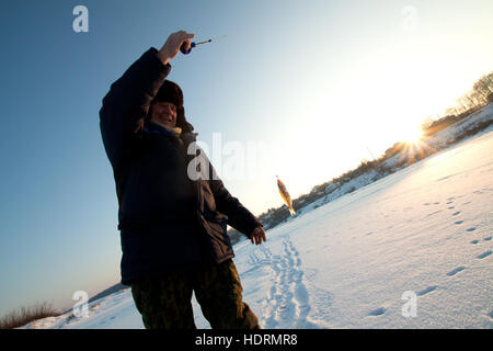 Tarusa, Russie - le 17 décembre 2010 : la pêche d'hiver. Pêcheur tenant un poisson pris sur l'hameçon dans les rayons du soleil. Banque D'Images