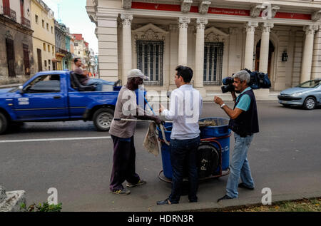 Une équipe de télévision cubaine rue entrevue le jour plus propre après la mort de Fidel Castro a été annoncé, comme un homme passe derrière assis sur une chaise dans le dos de Banque D'Images