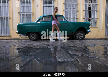 Lycéenne passe devant une vieille voiture classique avec de la rouille, stationné sur la rue pavée à La Havane Vieja, La Havane, Cuba. Banque D'Images