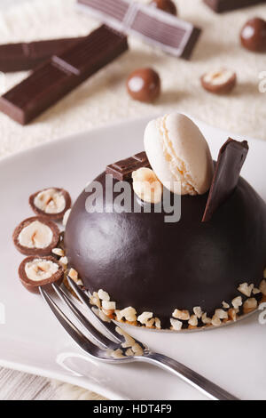 Beau gâteau au chocolat avec des noix, garni d'une assiette de macarons close-up vertical. Banque D'Images