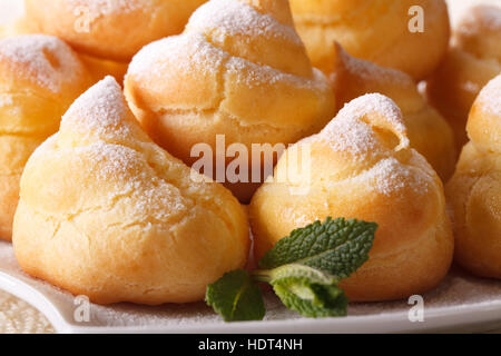 Profiteroles fraîche saupoudrée de sucre en poudre et la menthe macro sur une plaque horizontale. Banque D'Images