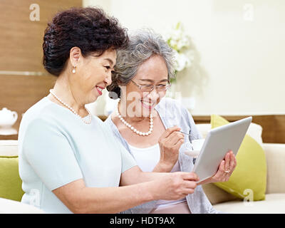 Vue latérale des deux senior Asian women sitting on couch prenant une aide selfies téléphone mobile, heureux et souriant Banque D'Images