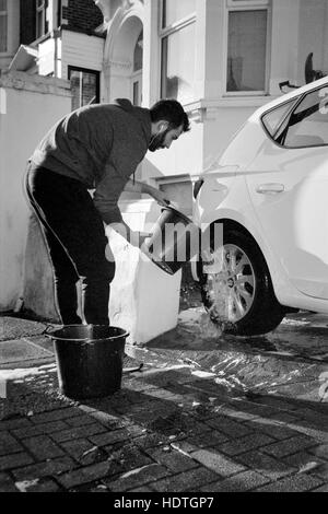 Un jeune homme voiture lavage à la main à l'aide d'un seau d'eau chaude england uk Banque D'Images