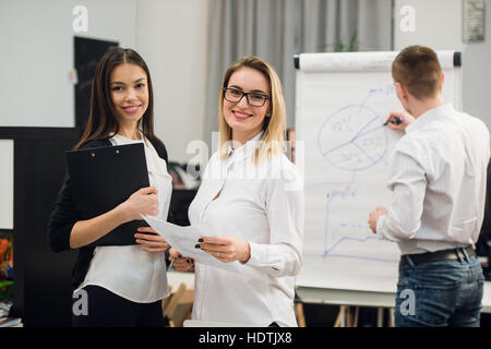 Deux belles des employés de bureau ayant conversation tandis que l'homme collègue dimensions stratégie d'entreprise sur un tableau. Banque D'Images